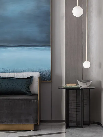 This image captures a quiet, minimalist corner of a residence. The design features a large, atmospheric blue painting, textured grey wall panels, and delicate globe pendant lights, creating a serene and artistic vignette.