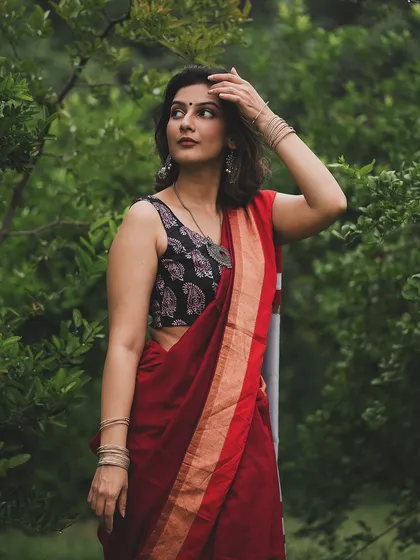 A full-length shot of a model in a red and black saree against a lush green background. This image highlights the elegance of the saree and its drape in a natural setting.