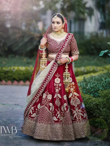 A full-length portrait showcasing the bride's magnificent wedding lehenga. Standing gracefully in a garden, she holds her kalire, embodying the timeless elegance of an Indian bride.