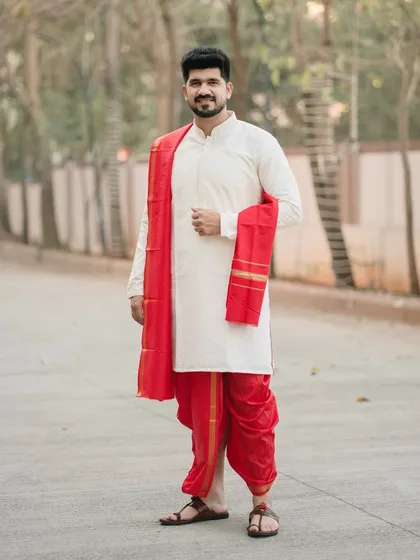 A classic portrait of a groom in traditional Marathi attire. The simple, clean background allows his vibrant red dhoti and serene expression to take center stage.