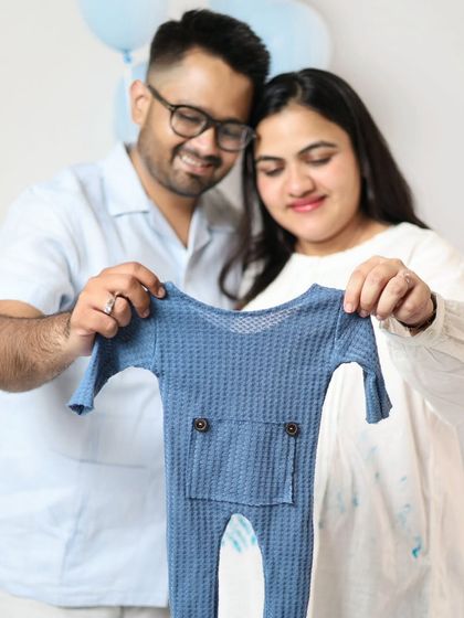 A close-up of the couple proudly showing off the little blue romper for their son. These detail shots are a lovely part of a gender reveal photoshoot.