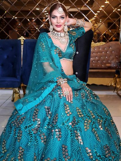 A full-length shot of a stunning turquoise lehenga. The makeup is kept bright and glamorous to match the vibrant color of the outfit, perfect for a sangeet or reception.