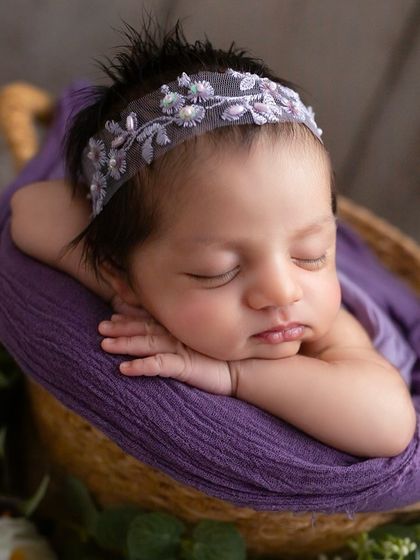 A close-up of three-week-old Samaya, sleeping peacefully. The purple wrap and embroidered headband add a touch of elegance to this classic newborn portrait.