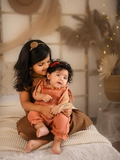 A tender moment between sisters during a five-month boho-themed milestone shoot. The warm, earthy tones and soft textures create a cozy and loving atmosphere.