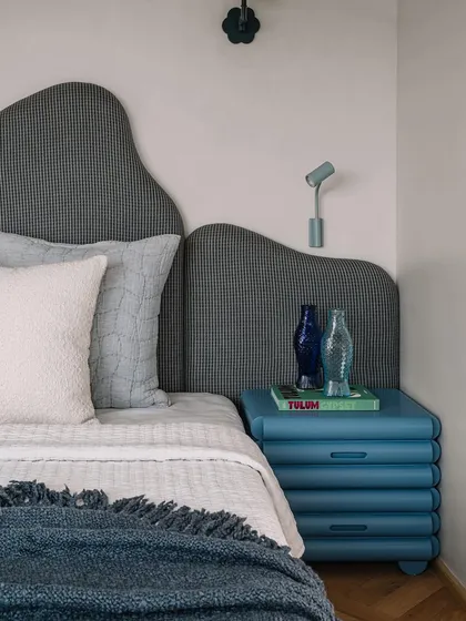 Another angle of the master bedroom, highlighting the unique blue bedside table and the textured, houndstooth-patterned headboard.
