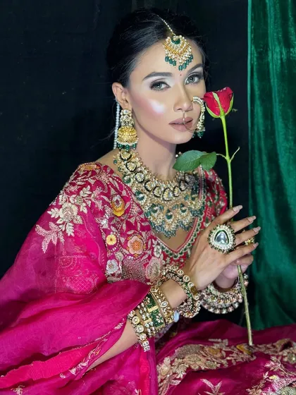 A romantic and classic bridal portrait. The single red rose adds a touch of timeless romance, while the makeup remains flawless with a focus on sharp, defined eyes and glowing skin.