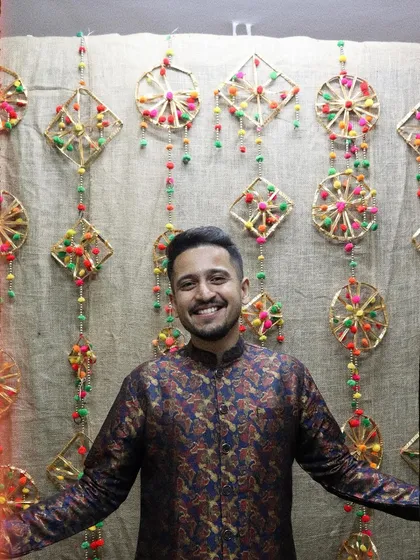 Posing with a smile against a backdrop of traditional, handmade decor. Embracing the festive vibes and desi swag.
