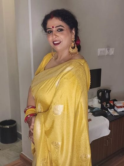 A guest at a daughter's wedding, looking beautiful in a yellow saree with classic makeup and a red lip.