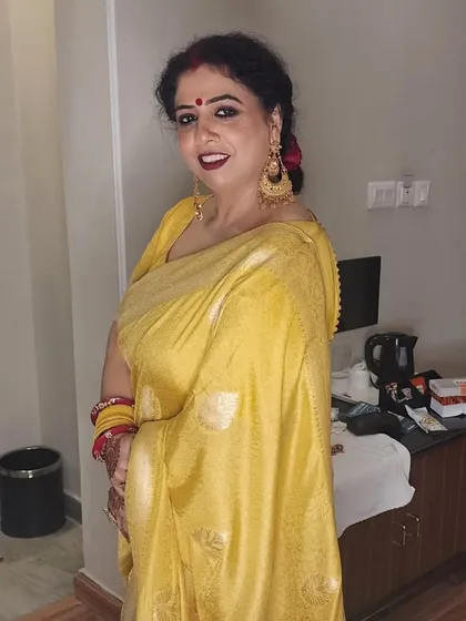 A guest at a daughter's wedding, looking beautiful in a yellow saree with classic makeup and a red lip.