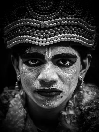 A black and white portrait of a performer preparing for a traditional ceremony. By stripping away color, the focus shifts entirely to the intense emotion in his eyes and the intricate details of his makeup, offering a direct glimpse into his spiritual state.
