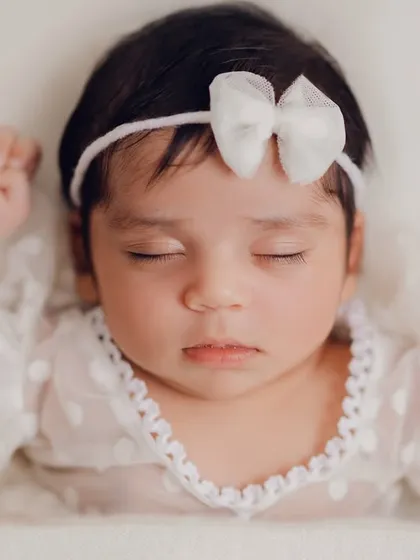 A close-up of a sleeping newborn, showcasing her delicate features and the soft lace of her dress. These simple, clean shots are all about capturing the pure innocence of a new life.