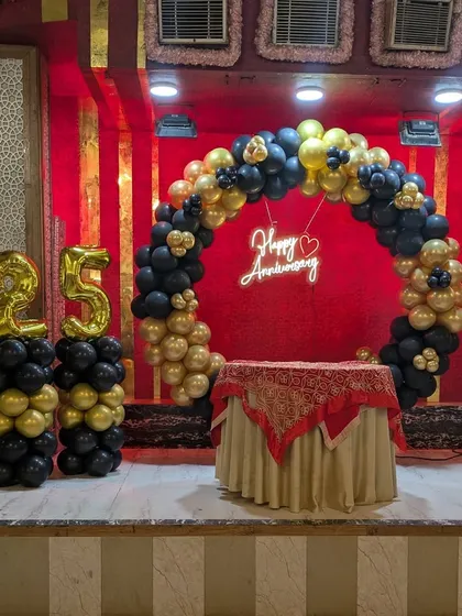 This 25th anniversary setup features a circular balloon arch in black and gold, with matching balloon pillars and large foil number balloons.