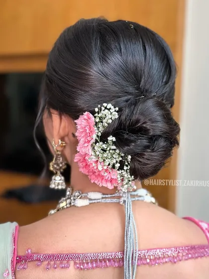 This sleek low bun is adorned with pink carnations and baby's breath. It's a classic choice for bridesmaids or wedding guests looking for an elegant floral hairstyle.
