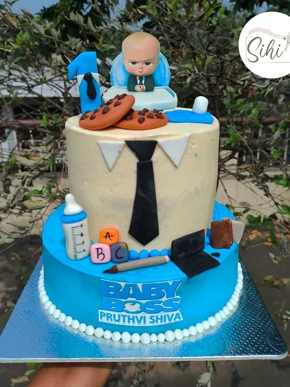 A two-tier cake for a "Baby Boss." This design is inspired by the movie Boss Baby and includes a fondant figurine, a tie, a laptop, and other fun, corporate-themed details.