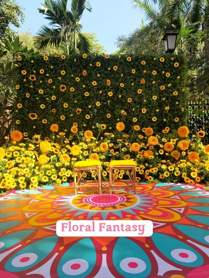 A "Floral Fantasy" Haldi setup with a wall of sunflowers and a colorful hand-painted rangoli-style floor, creating a picture-perfect spot.