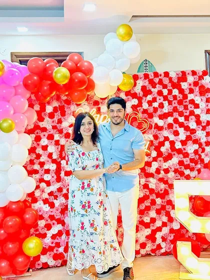 A happy couple celebrating their 5th anniversary with our decor. We created a beautiful photo backdrop using a red and white floral wall, complemented by a balloon garland and a light-up number '5'.