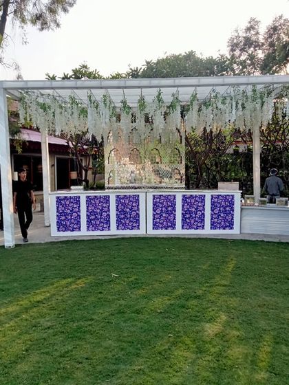 A stylish bar setup for a day wedding, with a floral-printed front and a canopy of hanging white wisteria.