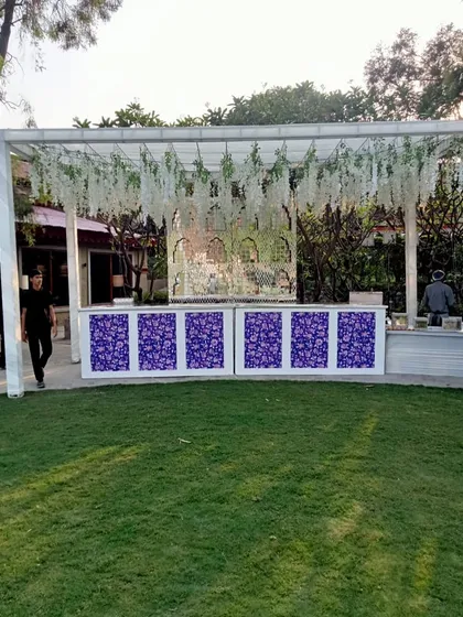 A stylish bar setup for an outdoor wedding, with a white frame, hanging wisteria, and a patterned purple and white front.