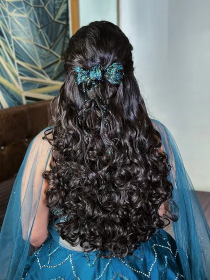 A fun and modern hairstyle with curly hair, a half-updo, and a sparkling blue bow accessory.