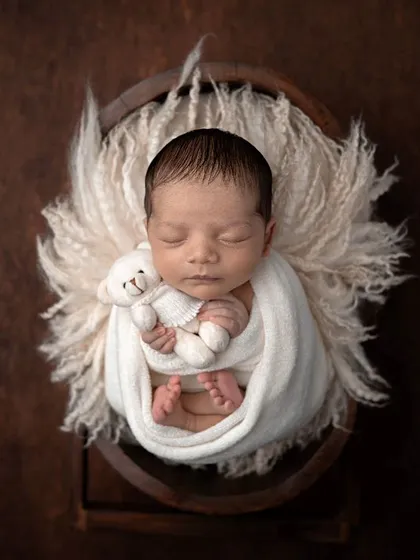 A newborn angel surrounded by white feathers and holding a tiny teddy. This overhead shot is pure, simple, and beautiful.