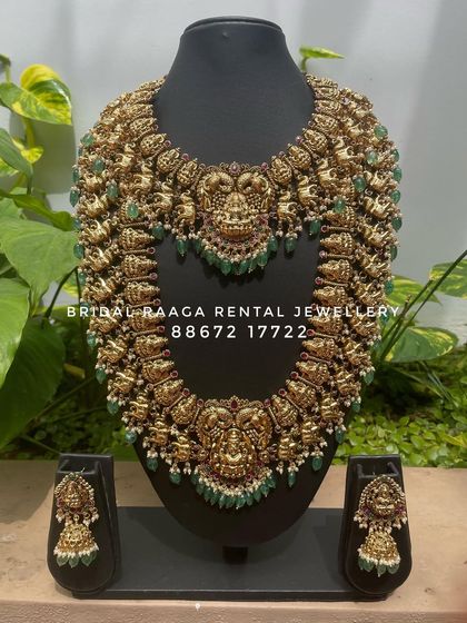 This grand bridal set features heavy carvings and is accented with green beads. It includes a statement choker, a matching long haram, and jhumkas, perfect for a majestic look.