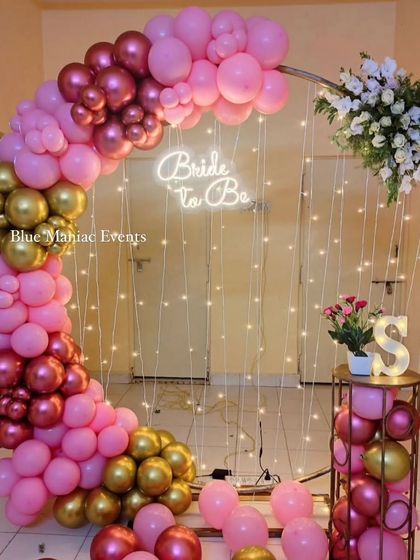 A chic 'Bride to Be' setup for a bridal shower. The decoration features a circular frame with a pink and gold balloon arch, a neon sign, and fairy lights.