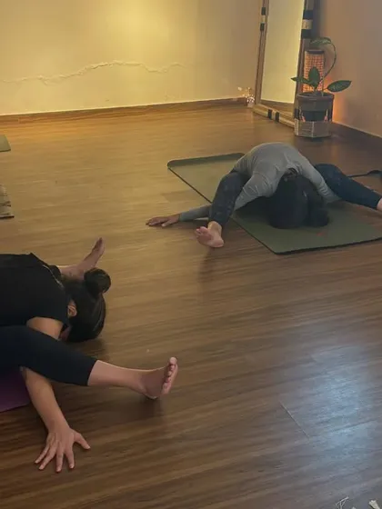 A class works on various hip-opening and forward-folding postures, each student moving at their own pace and depth.
