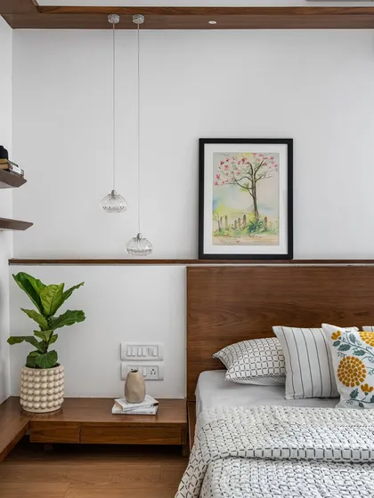 The bedroom in 'Pepper and Coffee' showcases a custom wooden bed with a floating nightstand and a continuous ledge for art and pendant lights.