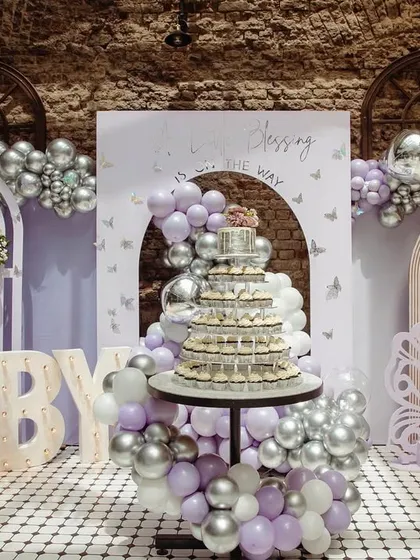 The main decor setup for our butterfly-themed baby shower, featuring a dessert table, marquee 'BABY' lights, and arches adorned with lavender balloons.