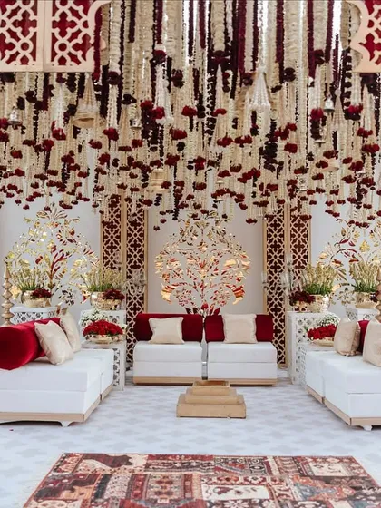 The main stage area for the 'Laal Ishq' wedding, featuring a breathtaking ceiling of hanging rajnigandha and rose garlands. The white seating with red accents provides a beautiful contrast to the rich floral decor.