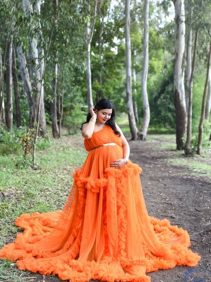 A stunning portrait of a mom-to-be in a vibrant orange gown, set against a backdrop of eucalyptus trees.