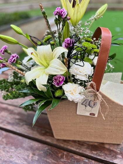 A stylish and elegant 40th birthday gift for him. The jute basket holds a beautiful arrangement of lilies and carnations, proving that floral gifts can be perfectly suited for men.