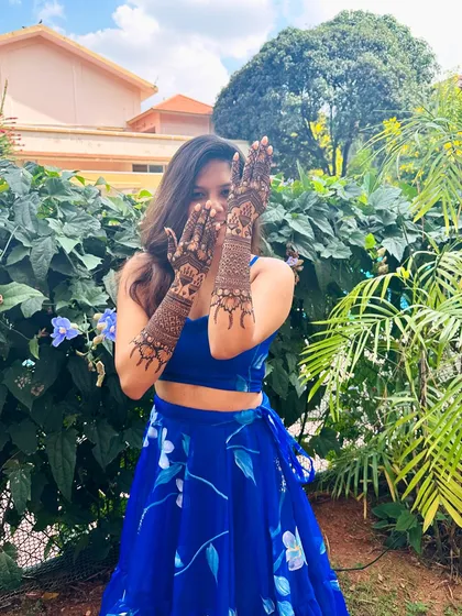 A client in a vibrant blue lehenga, her hands adorned with a beautiful elephant and floral mehndi design.