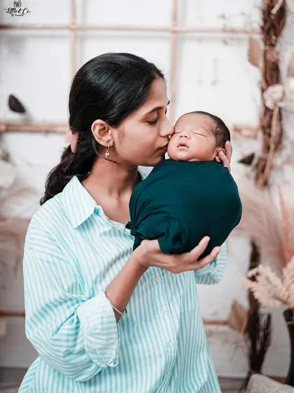 A mother's gentle kiss for her sleeping newborn. This photo highlights the serene bond between mother and child, set against our warm, rustic studio backdrop.