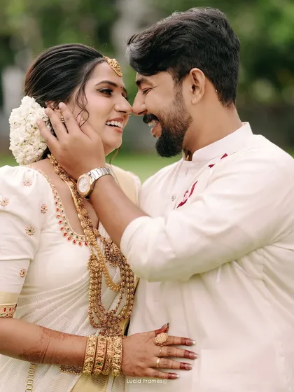 The beautiful smiles of a newly married couple, captured in a close-up that highlights the bride's traditional Kerala jewelry and the groom's loving touch.