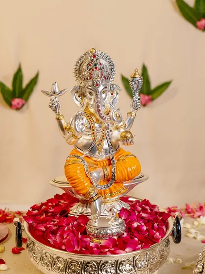 This silver-plated Ganesha idol, adorned with vibrant orange dhoti and intricate jewelry, is a celebration of divine energy. The craftsmanship captures his powerful form, ready to bless your home with success.