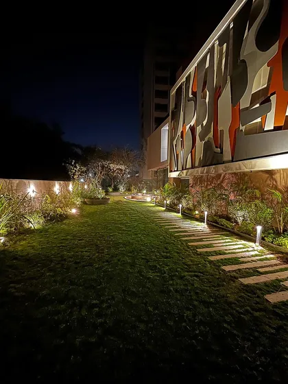 A wide view of the 'Framed Austerity' garden at night. The illuminated pathway leads the eye through the space, creating a serene and almost magical atmosphere where light and shadow play a crucial role.