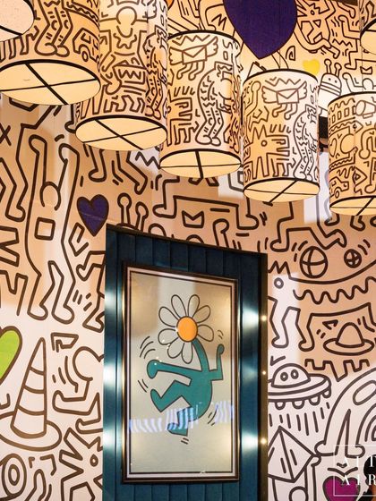 A detail of the Keith Haring room, showing the interplay between the doodled walls, custom lampshades, and framed artwork. The design creates a completely immersive environment that feels like stepping inside one of the artist's creations.