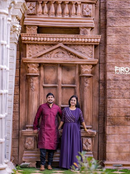 A couple stands before a grand, stone-carved doorway, a backdrop that adds a sense of history and importance to the photograph.