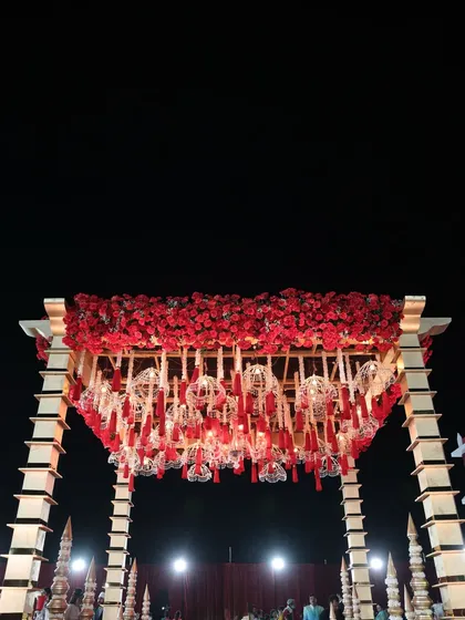 The mandap structure, showcasing its golden pillars and a canopy of red florals, stands as a testament to our ability to create large-scale, impactful decor.