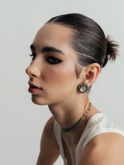 A beautiful profile shot highlighting a set of vintage-style earrings and a matching choker. The model's slicked-back hair ensures the jewelry is the main focus.
