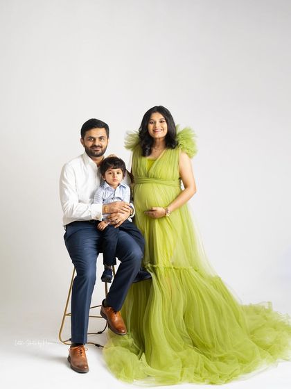 This expecting mother looks absolutely radiant in a vibrant green gown. Posed with her husband and son, this studio portrait is a stylish and happy celebration of their growing family.
