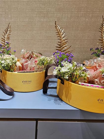 A wider view of the hampers designed for Entisi Chocolatier. The consistent use of golden ferns and soft florals creates a cohesive and sophisticated look for the brand's gifting needs.