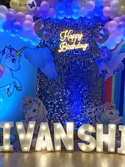 A magical unicorn theme for a first birthday. This enchanting setup features a shimmer wall, pastel rainbow balloon arch, unicorn cutouts, and large marquee letters for the name and number "1".