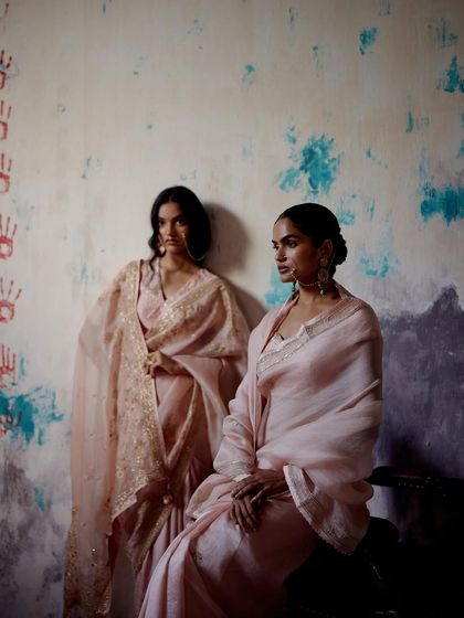 Models in soft, pastel pink sarees with delicate gold embroidery and borders, embodying a sense of quiet royalty.