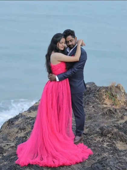 An epic pre-wedding shot on a cliffside. The vibrant pink gown provides a stunning pop of color against the blue ocean and sky.