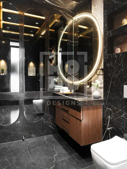 A large, backlit oval mirror brings a soft glow to this moody black marble bathroom. It provides excellent task lighting while enhancing the room's luxurious atmosphere.