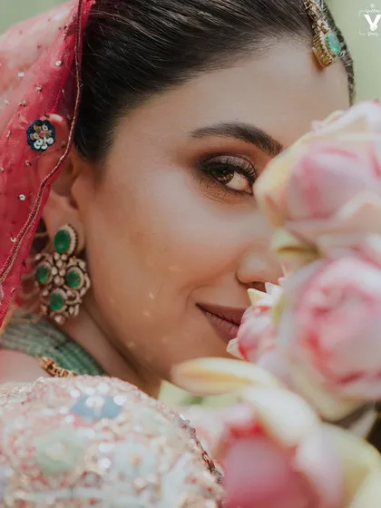 A beautiful close-up of the bride peeking through a bouquet of pink roses. This soft and romantic portrait highlights her stunning eye makeup and the delicate details of her look.