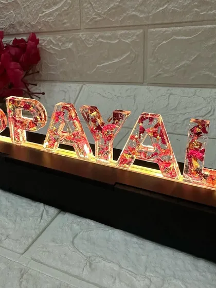 A close-up on the letters, showing the intricate detail of the preserved red flowers and gold flakes within the resin.