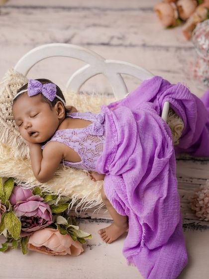 A royal slumber. This baby is sleeping peacefully in her purple lace outfit, surrounded by flowers and elegant props.
